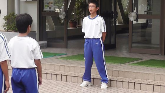 体操服を着た男の子が、手を後ろに組み生徒の前に立っている写真