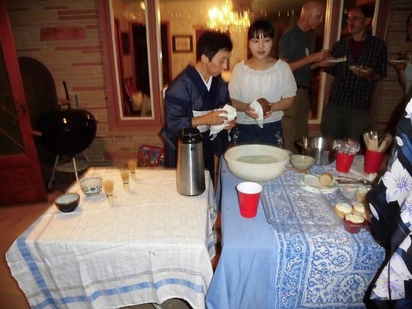 机の上には茶道の道具が用意され、細野先生と女性が器を拭いている写真