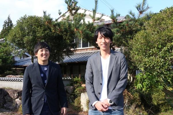紺色のジャケットを着た米田さんとグレーのジャケットを着た渡辺さんが青空の下、民家の前で写しているツーショット写真