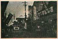 ネオンによって店の看板と道路が照らされている。また道には自動車が走っている。